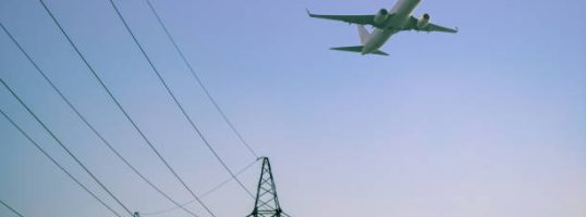 High voltage electricity power line towers against the sky. Airplane.